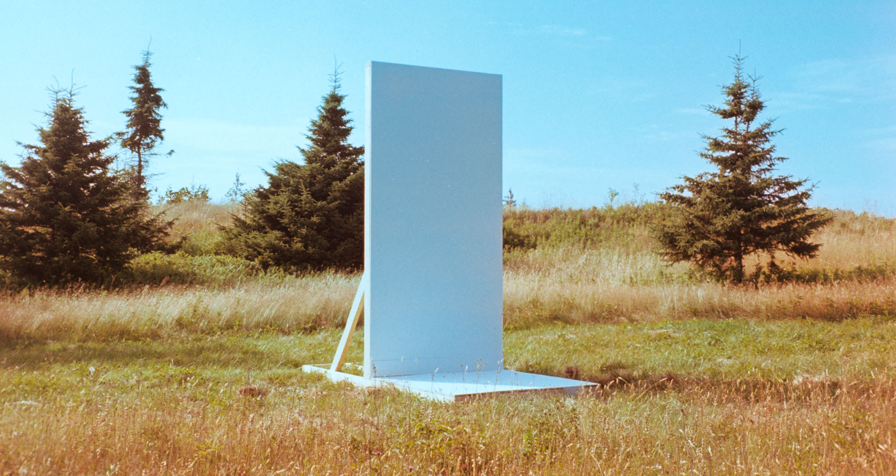 a chunk of white wall and white floor in the middle of a grassy field